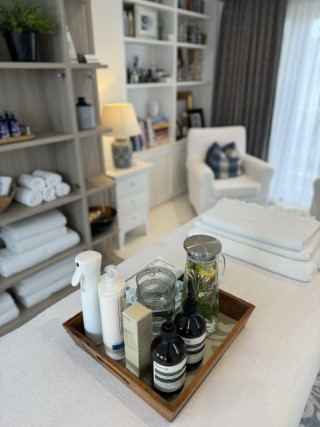 A tray on a massage table with a water pitcher with herbs and lemon.  In the background, clean, white towels and a comfortable armchair.